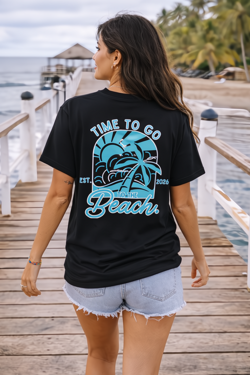 Woman in black "Time To Go To The Beach" 2026 graphic tee and denim shorts walking on a pier.