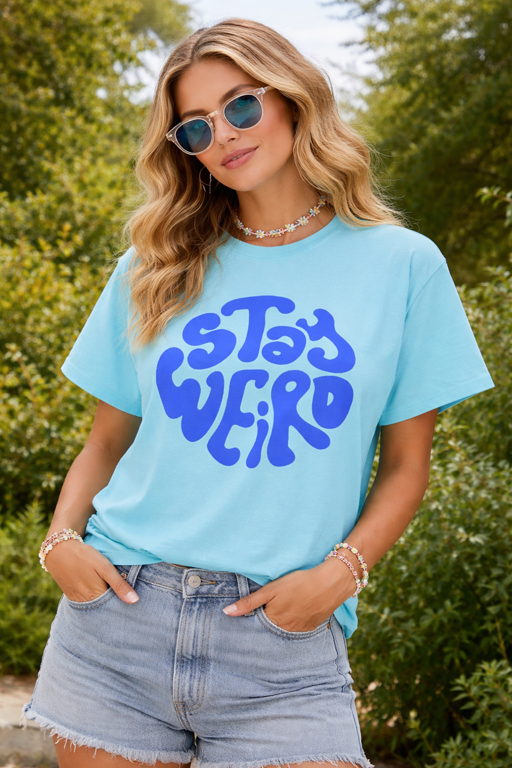 Woman wearing a light blue t-shirt with 'Stay Weird' text outdoors.