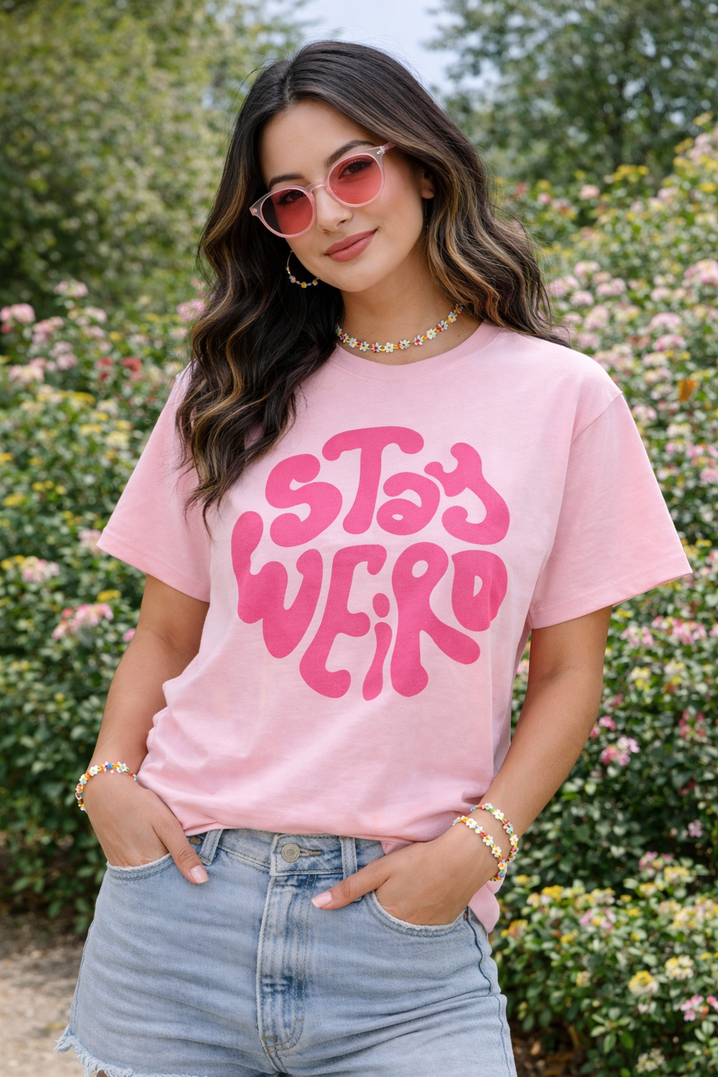 Woman wearing a pink 'Stay Weird' t-shirt in a garden setting