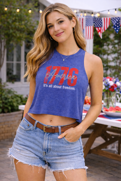 Woman wearing a blue crop top with '1776 It's all about freedom' text, standing outdoors.