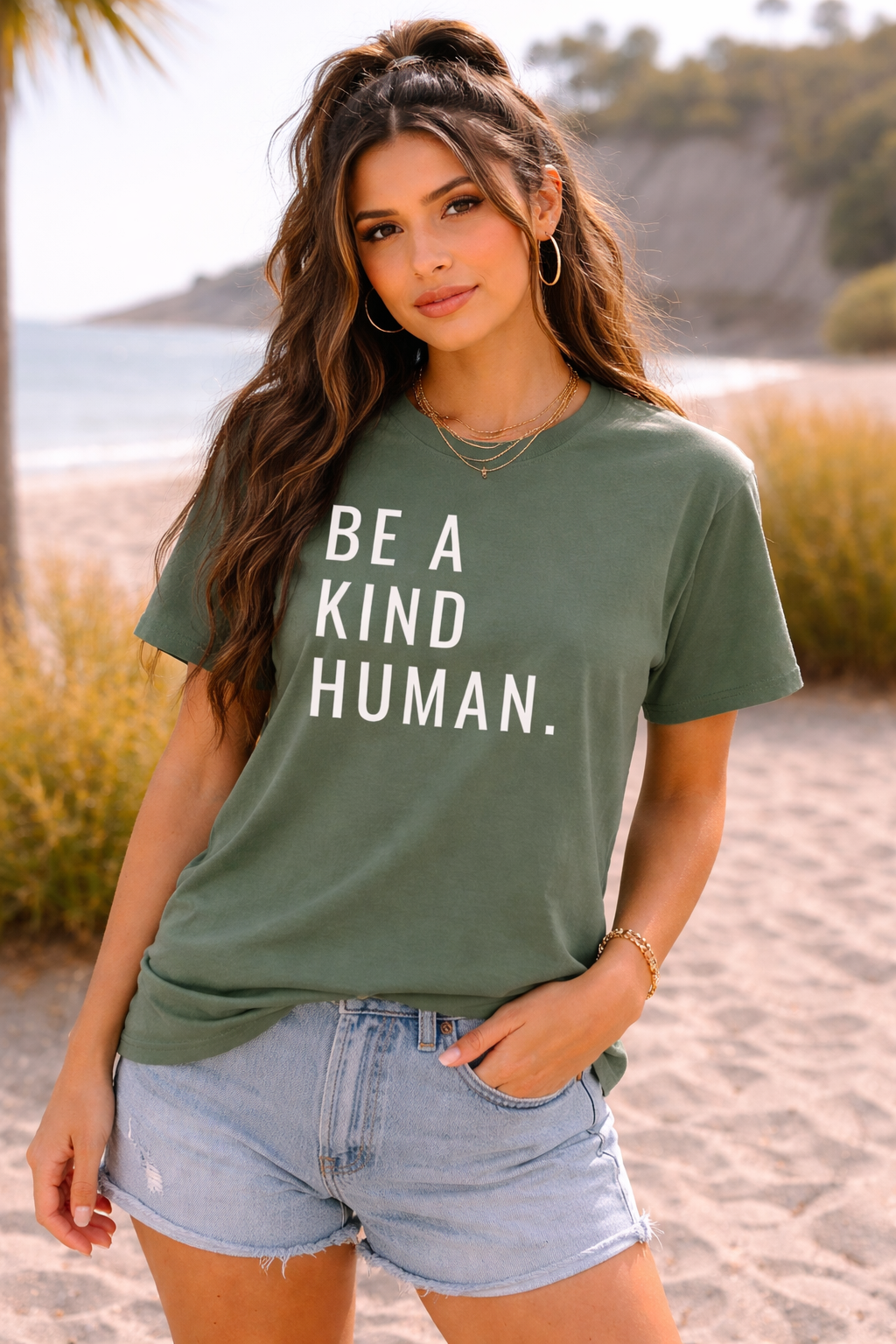Woman wearing a green t-shirt with 'Be a Kind Human' text on a beach.