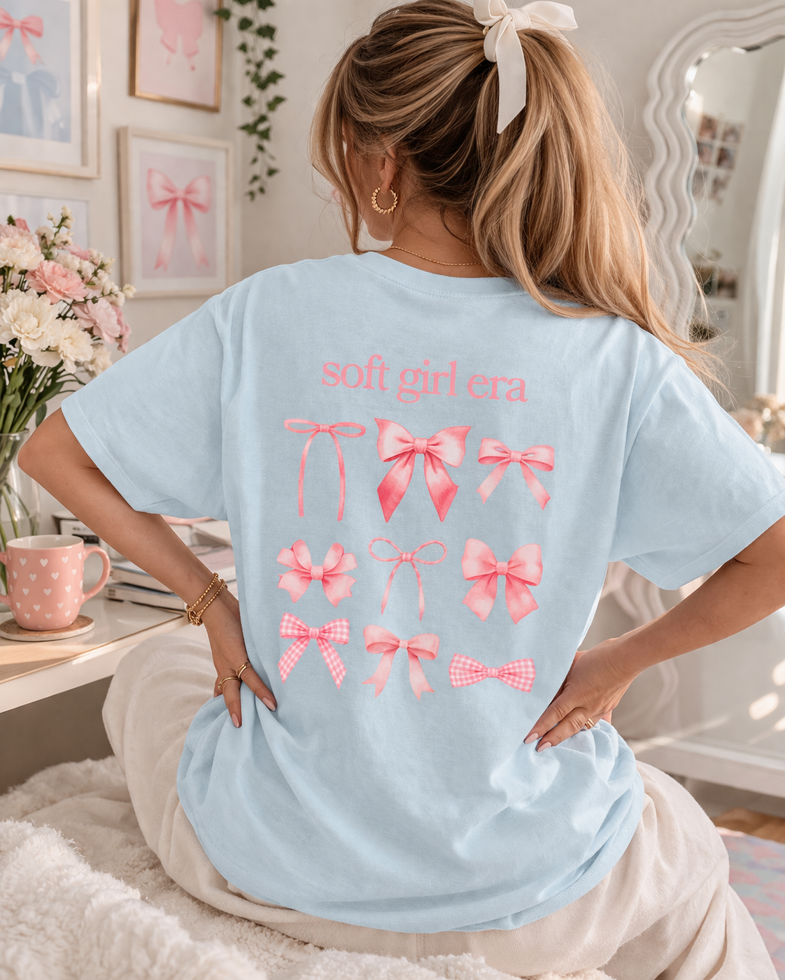 Person wearing a light blue t-shirt with pink graphics and text in a cozy room.