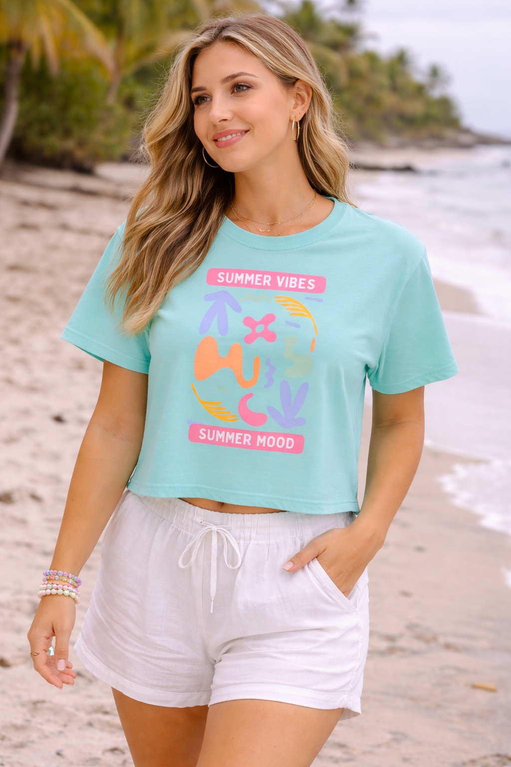 Woman wearing a light blue t-shirt with colorful graphics and text on a beach.