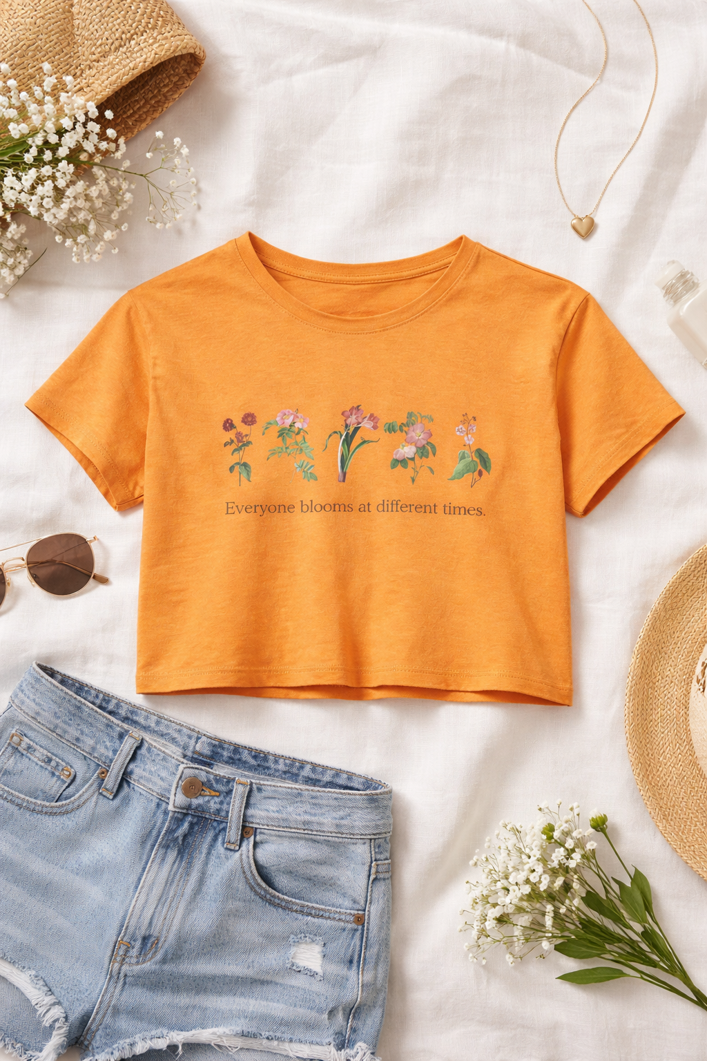 Orange t-shirt with floral design and text on a white background with denim shorts and flowers.