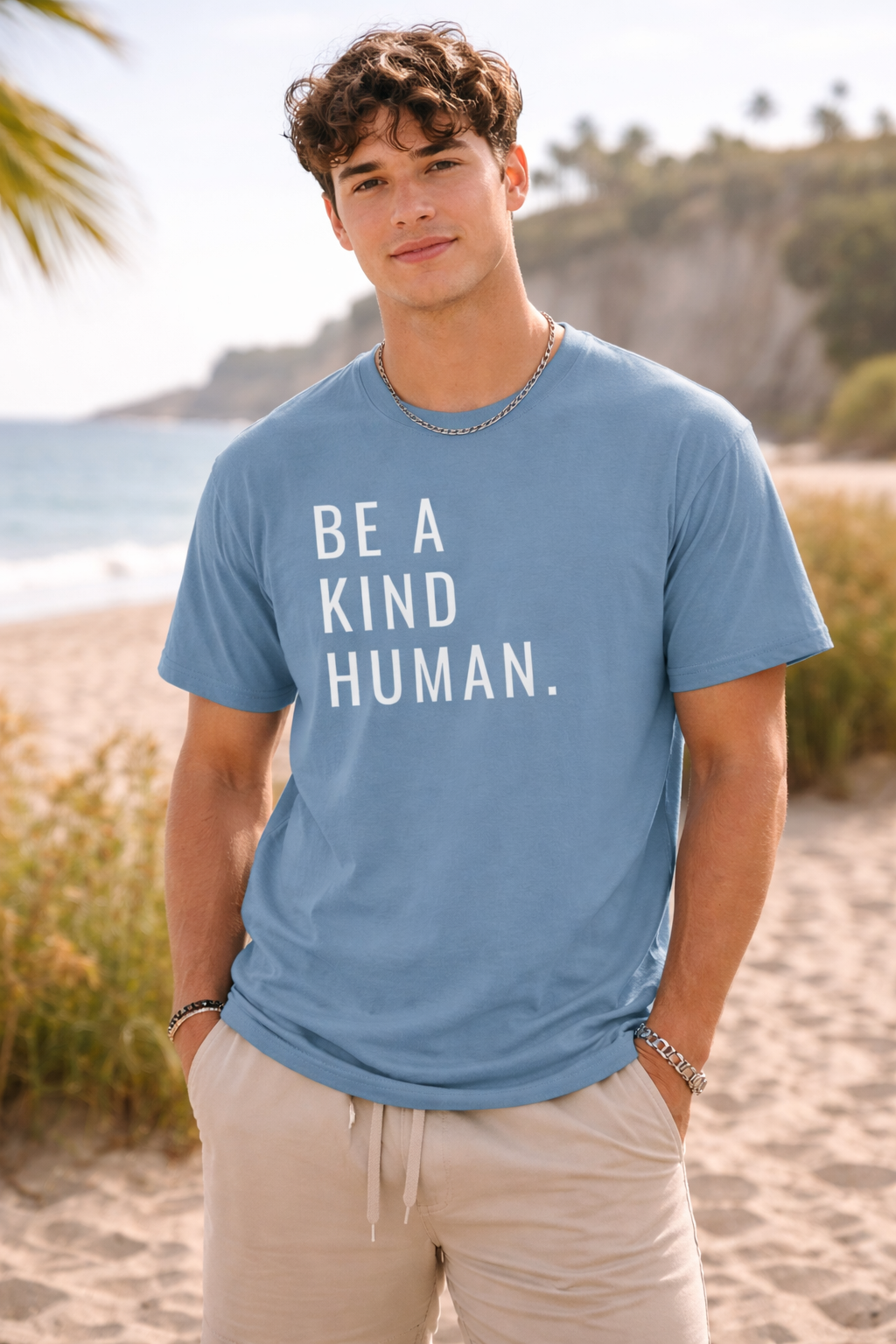 Man wearing a blue t-shirt with 'Be a Kind Human' text on a beach