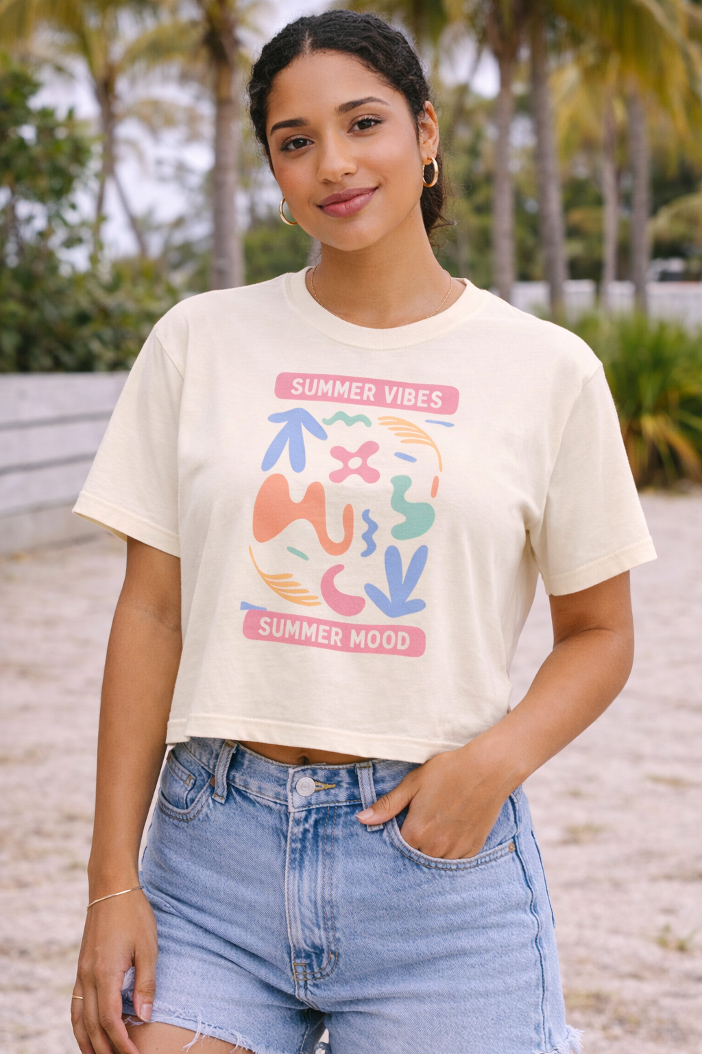 Woman wearing a white t-shirt with colorful graphics and text, standing on a beach.