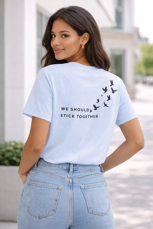 Woman wearing a light blue t-shirt with text and bird design outdoors