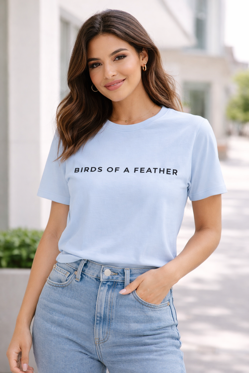 Woman wearing a light blue t-shirt with 'Birds of a Feather' text, standing outdoors.