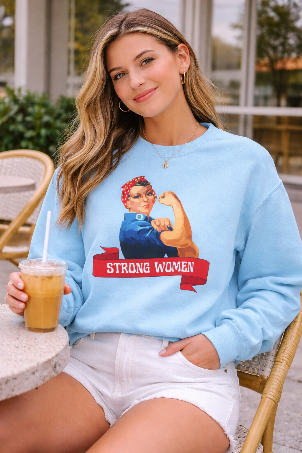 Woman wearing a light blue sweatshirt with a graphic design and text, sitting outdoors.