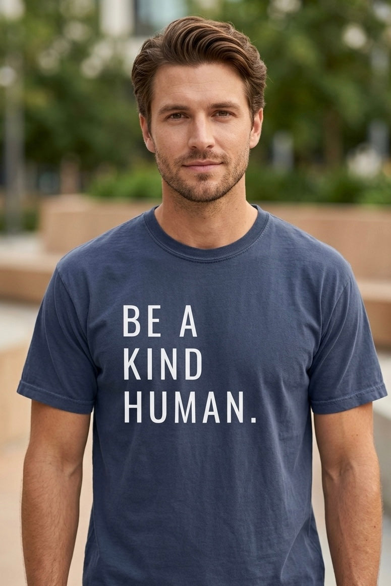 Man wearing a navy blue t-shirt with 'BE A KIND HUMAN.' text outdoors.