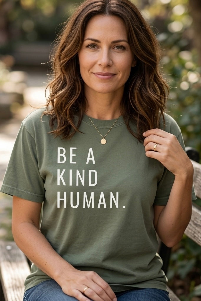 Woman wearing a green t-shirt with 'Be a Kind Human' text, sitting outdoors.