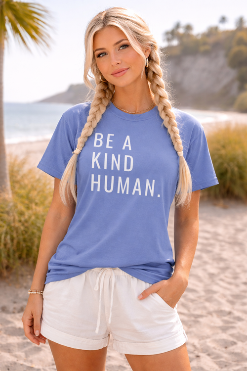 Woman wearing a blue t-shirt with 'Be a Kind Human' text on a beach.