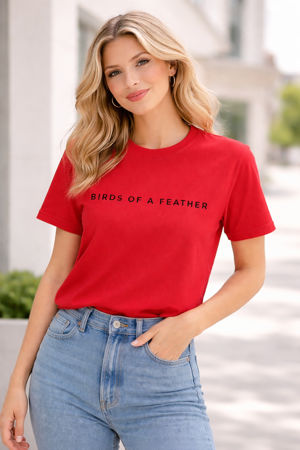 Woman wearing a red t-shirt with 'BIRDS OF A FEATHER' text, standing outdoors.