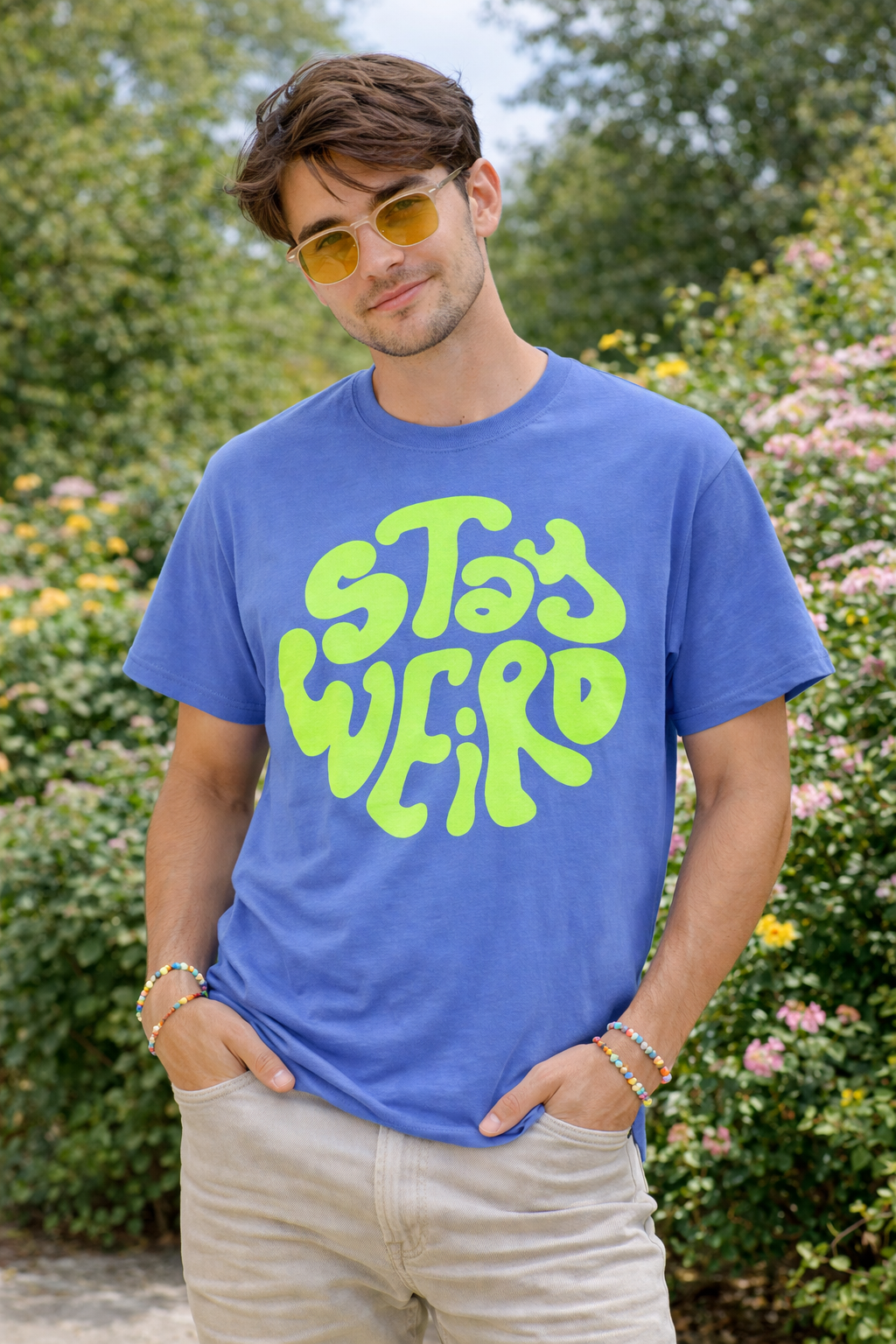 Man wearing a blue t-shirt with 'Stay Weird' in green text, standing outdoors.
