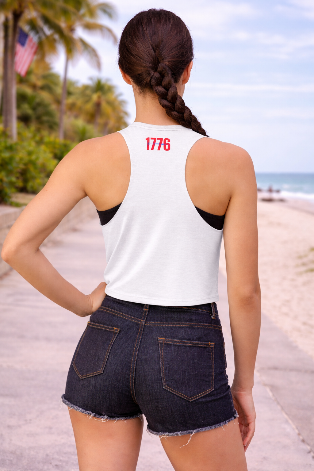 Person wearing a white tank top with '1776' on the beach