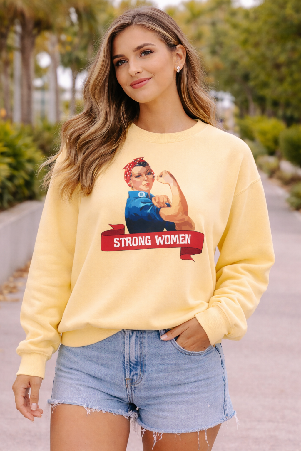 Woman wearing a yellow sweatshirt with a graphic design and text outdoors.